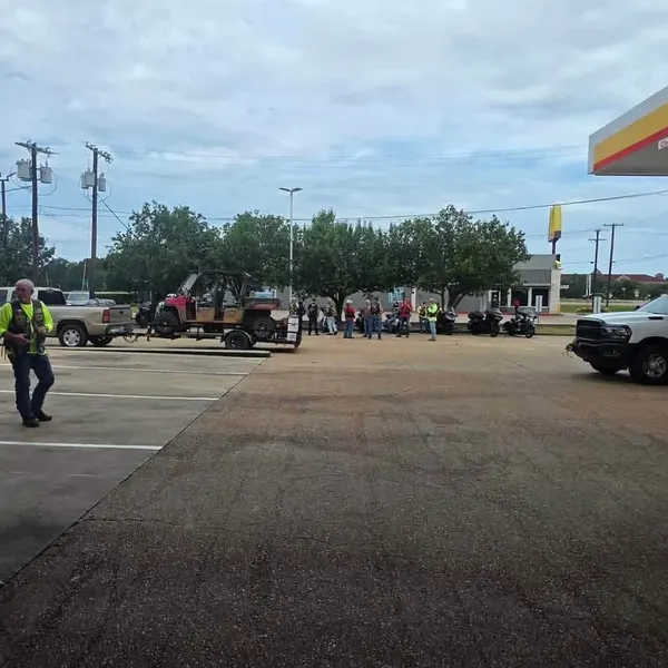 Riders and support vehicles gathered in a service station lot before departure.