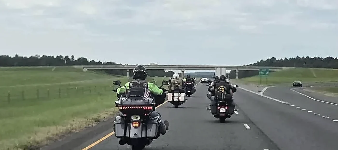 Motorcycles riding in formation along a divided highway, escorting a veteran's remains.