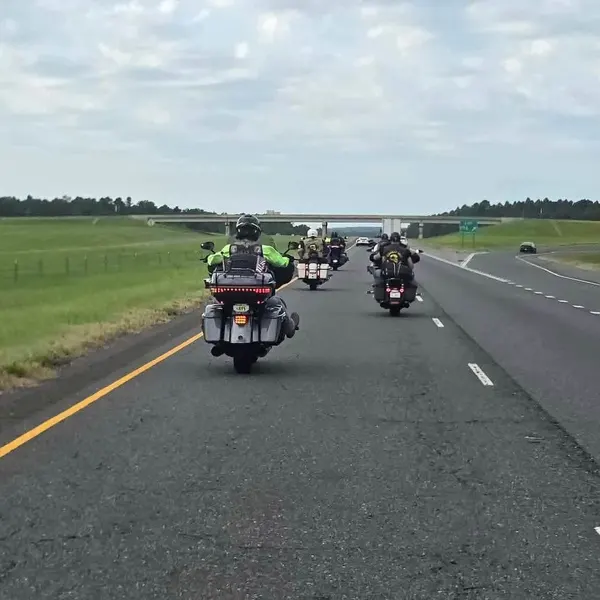 Motorcycles riding in formation along a divided highway under a partly cloudy sky.