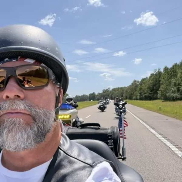 Rider's view of the escort ahead on a two-lane road lined with trees.