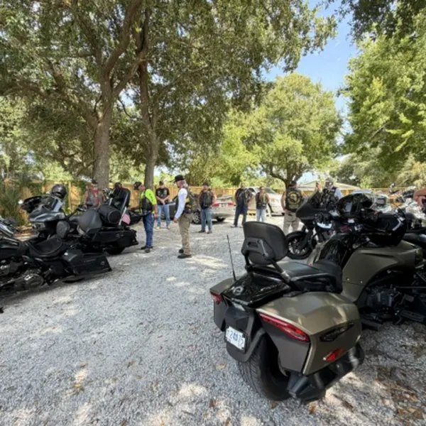 Motorcycles parked under oak trees with riders standing nearby.