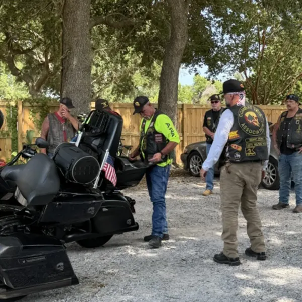 Riders in Combat Veterans Motorcycle Association vests standing together beside parked motorcycles.